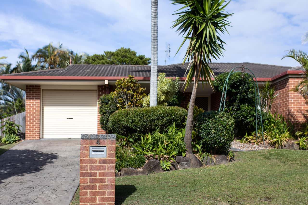 A brick home, with a bit of grass and greenery, a single car garage and a number 4 on the letterbox.