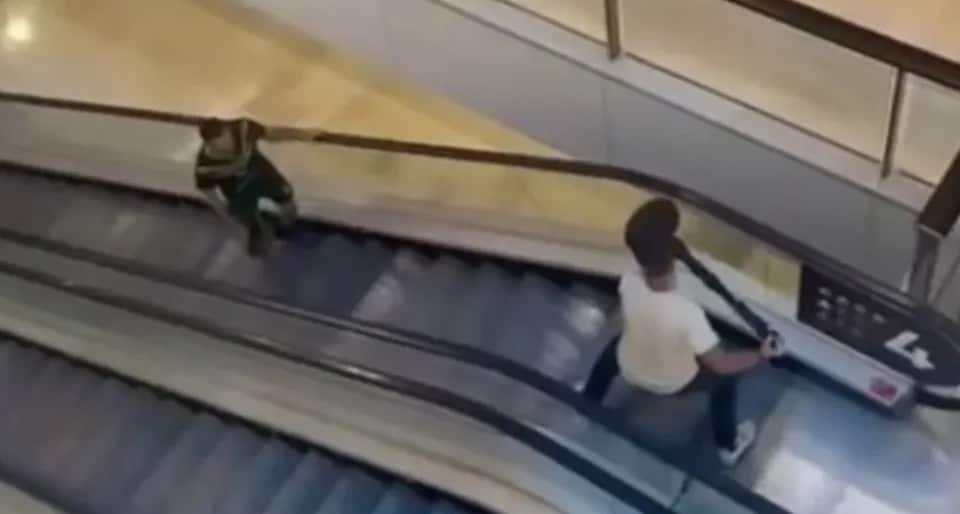 A man at the top of an escalator holding up a bollard as a man with a knife approaches