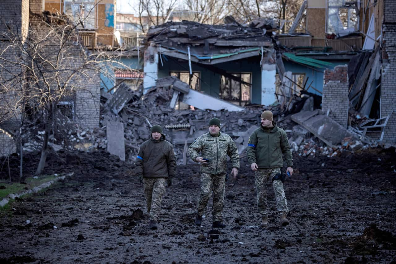 Three Ukrainian soldiers in front of destroyed buildings in the Donbas region.