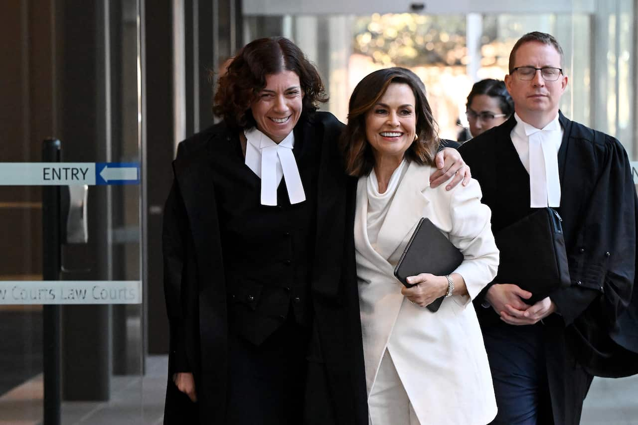 A woman in barrister's clothes walks with her arm around another woman wearing a white suit. 