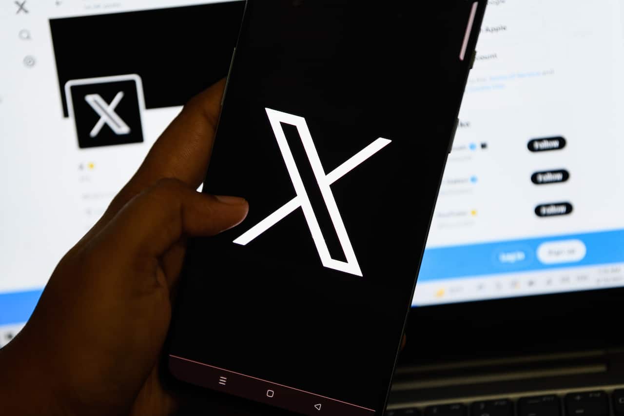 A person holding a smartphone with the X Corp logo on the screen.