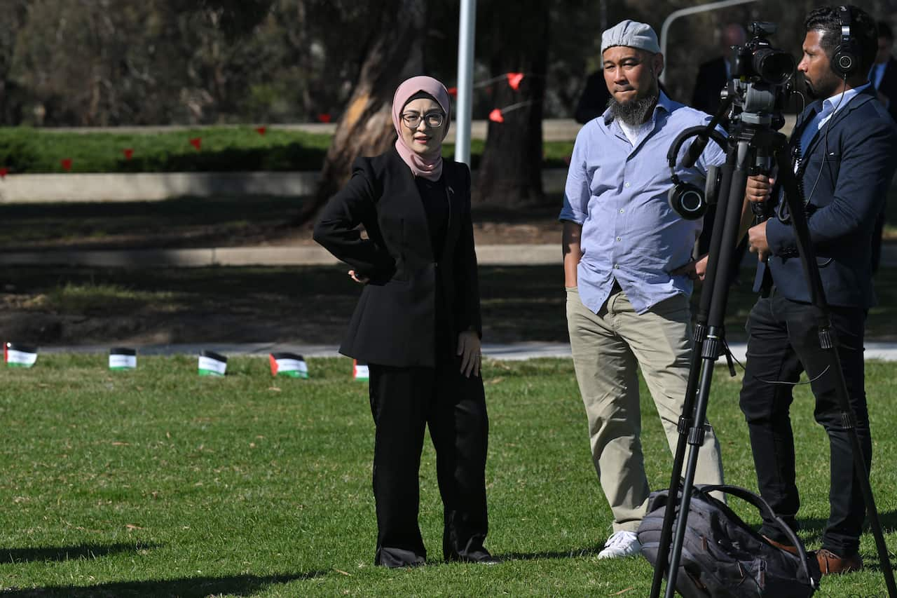 Three people stand around a camera on a tripod