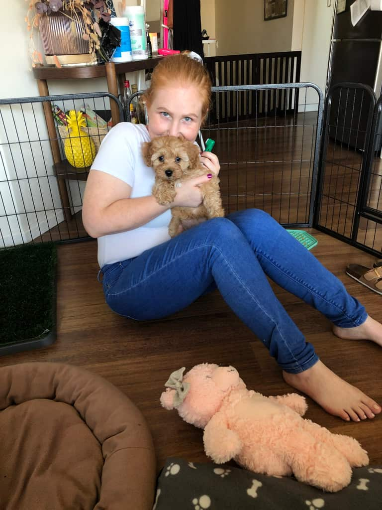 A woman sitting on the floor in a house. She is holding a puppy and smiling.