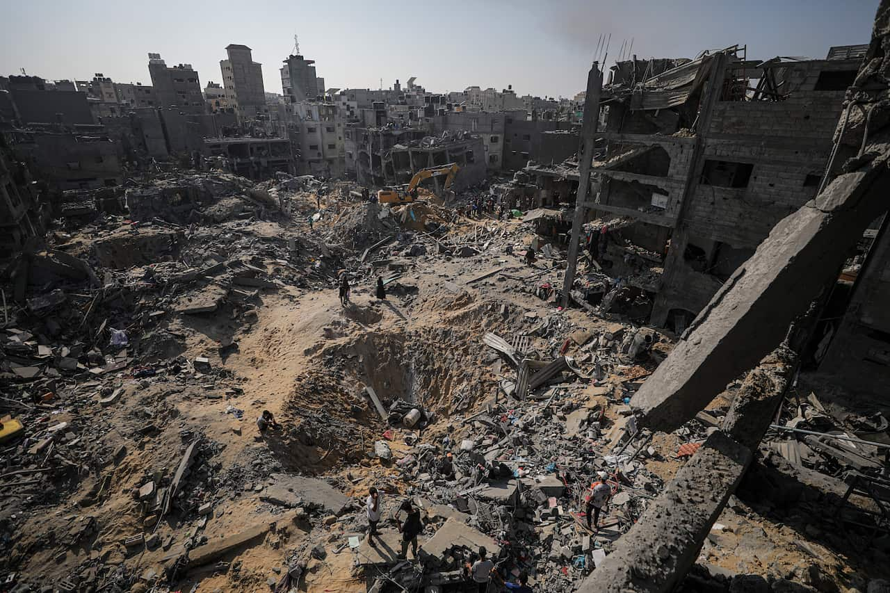 A bomb crater is seen among a heavily damaged area of buildings.