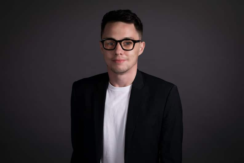 A man smiling with glasses and a black blazer and white shirt