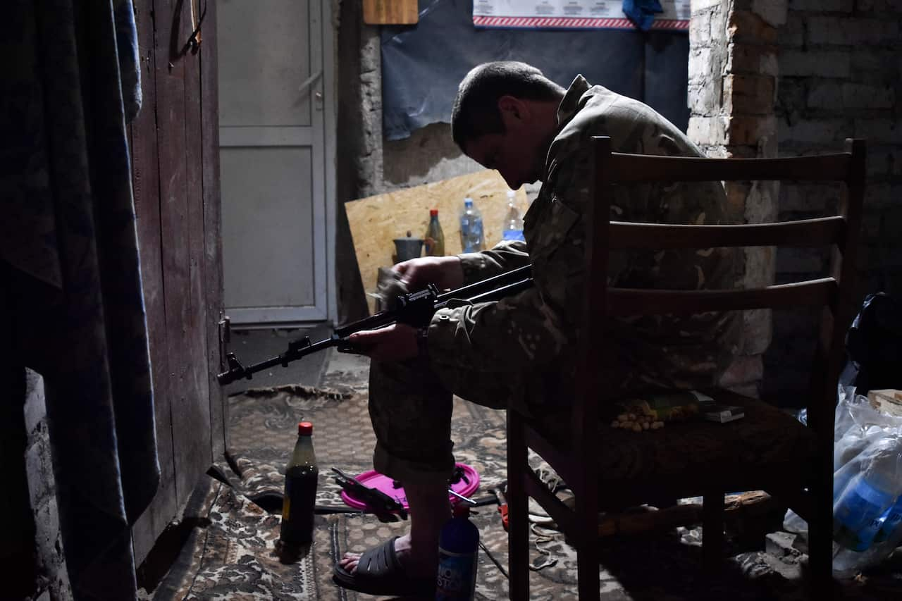 A Ukrainian soldier sits in a chair cleaning his rifle.