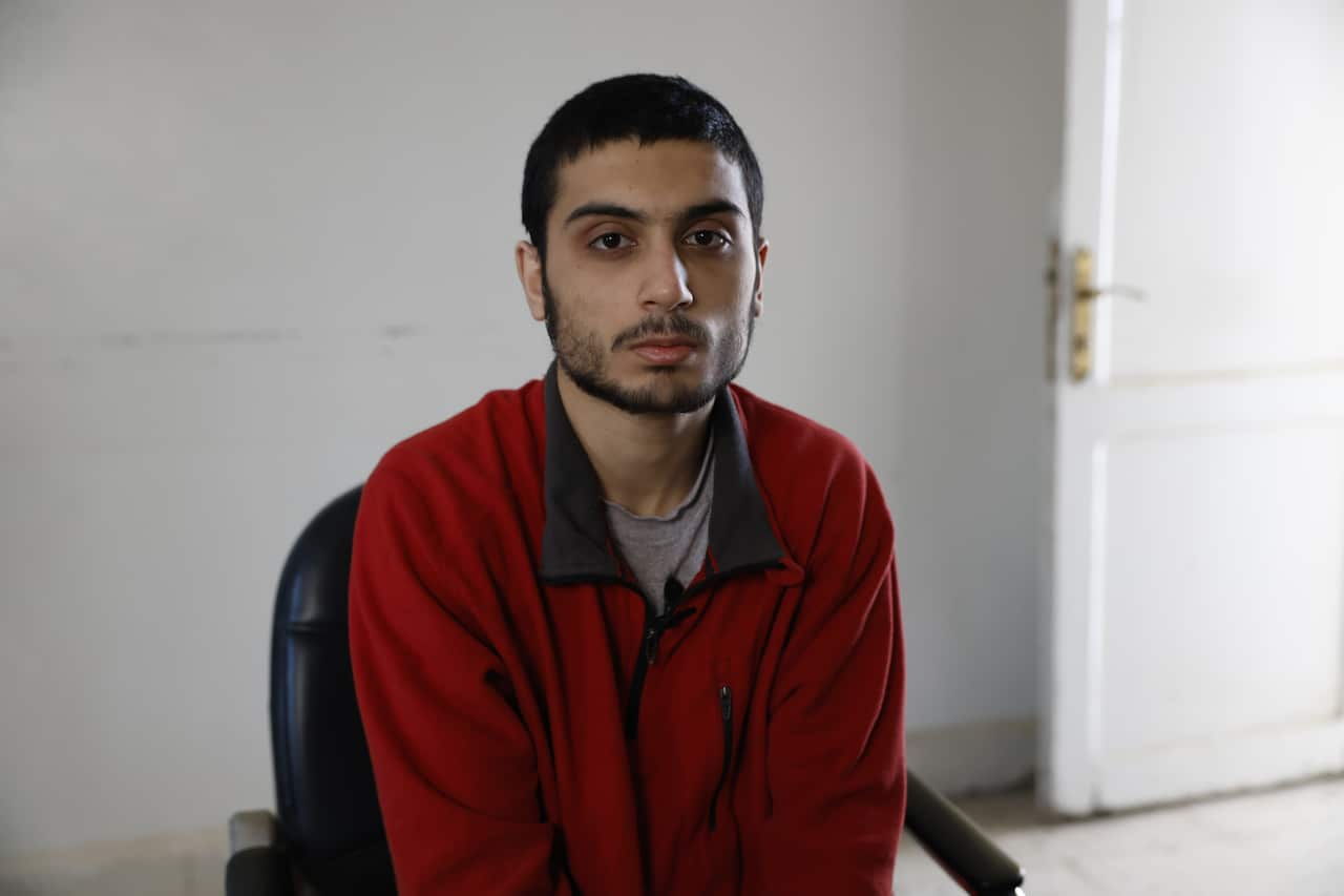 A young man in a red fleece looks at the camera with a serious expression on his face