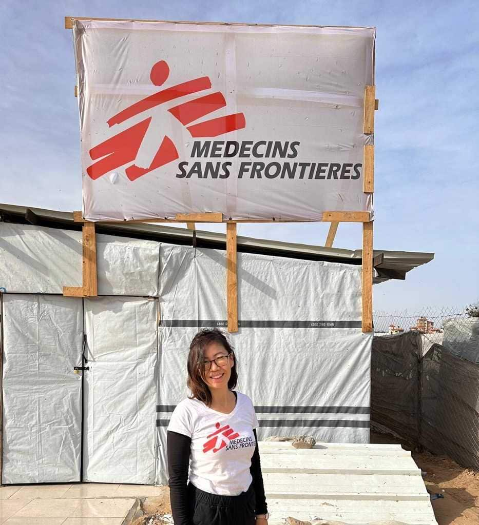 Scarlett Wong standing in front of a makeshift clinic with a sign that has the Medecins Sans Frontieres logo.