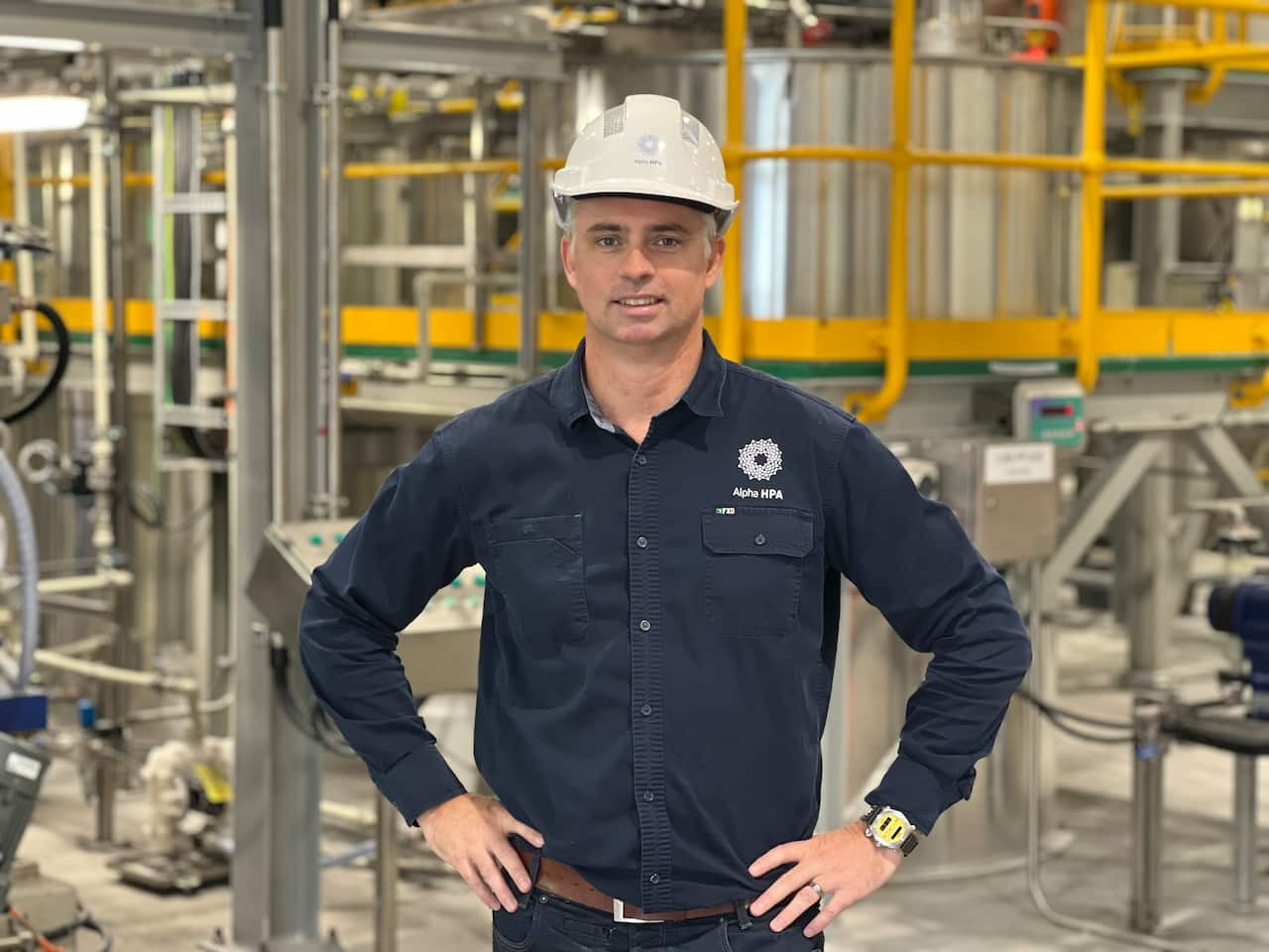 A man in a hard hat stands in an industrial site.