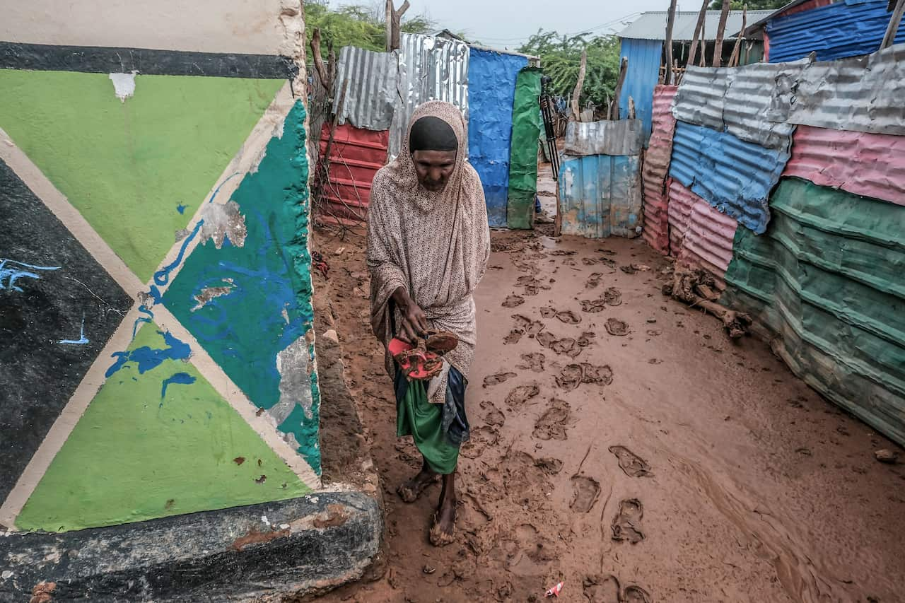 A woman walking through mud, between ramshackle dwellings.