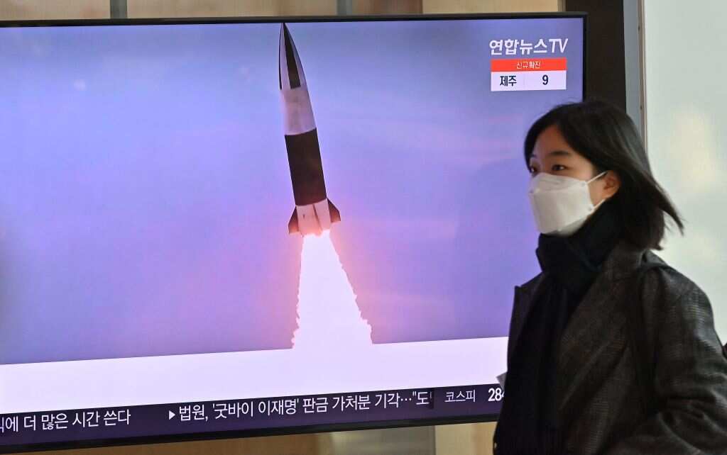 A woman walks past a television screen showing a news broadcast with file footage of a North Korean missile test.