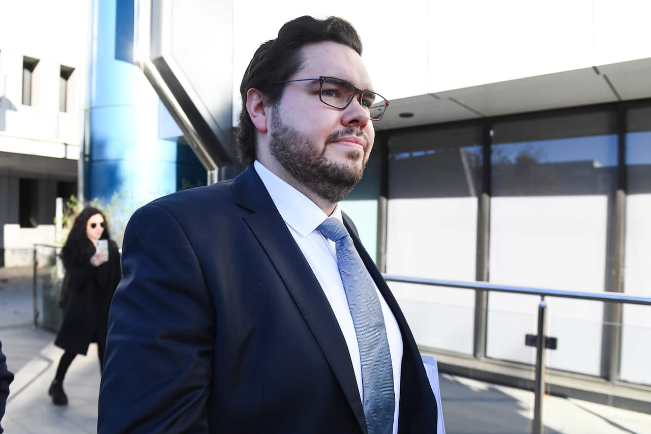 A man in a dark suit with neat dark hair walks outside a court building.