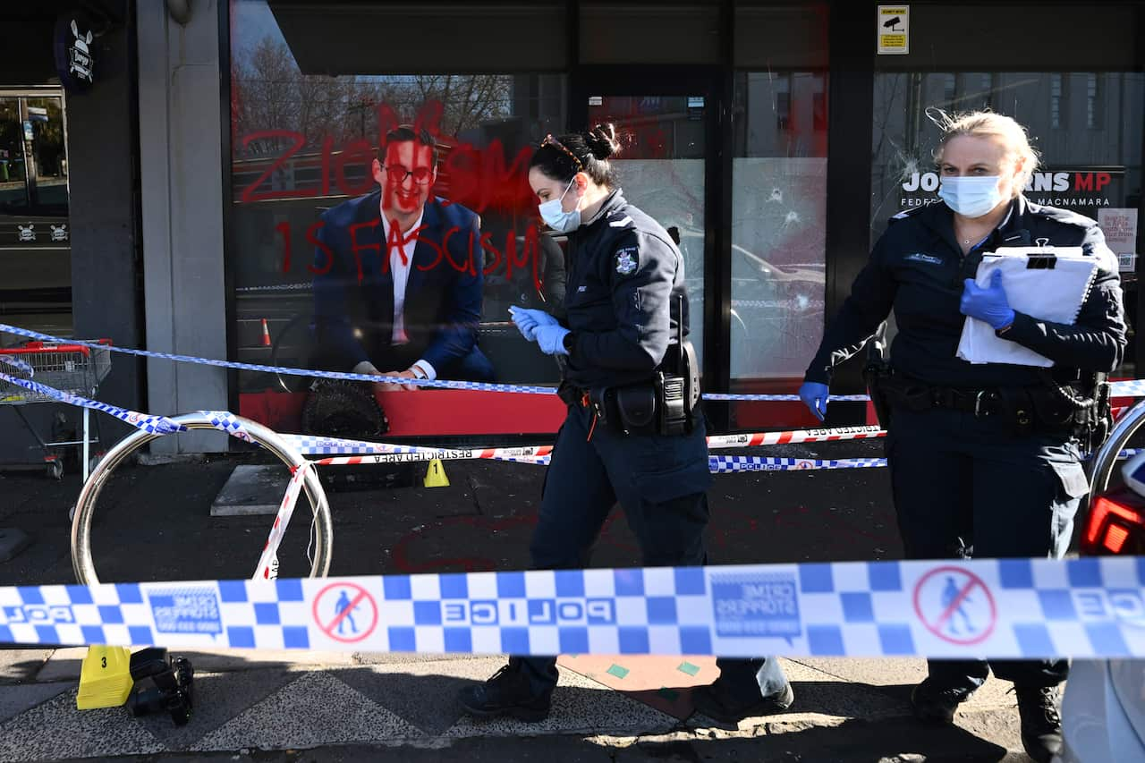 Red painted graffiti on an office window. There are two policewomen and police tape in the foreground 