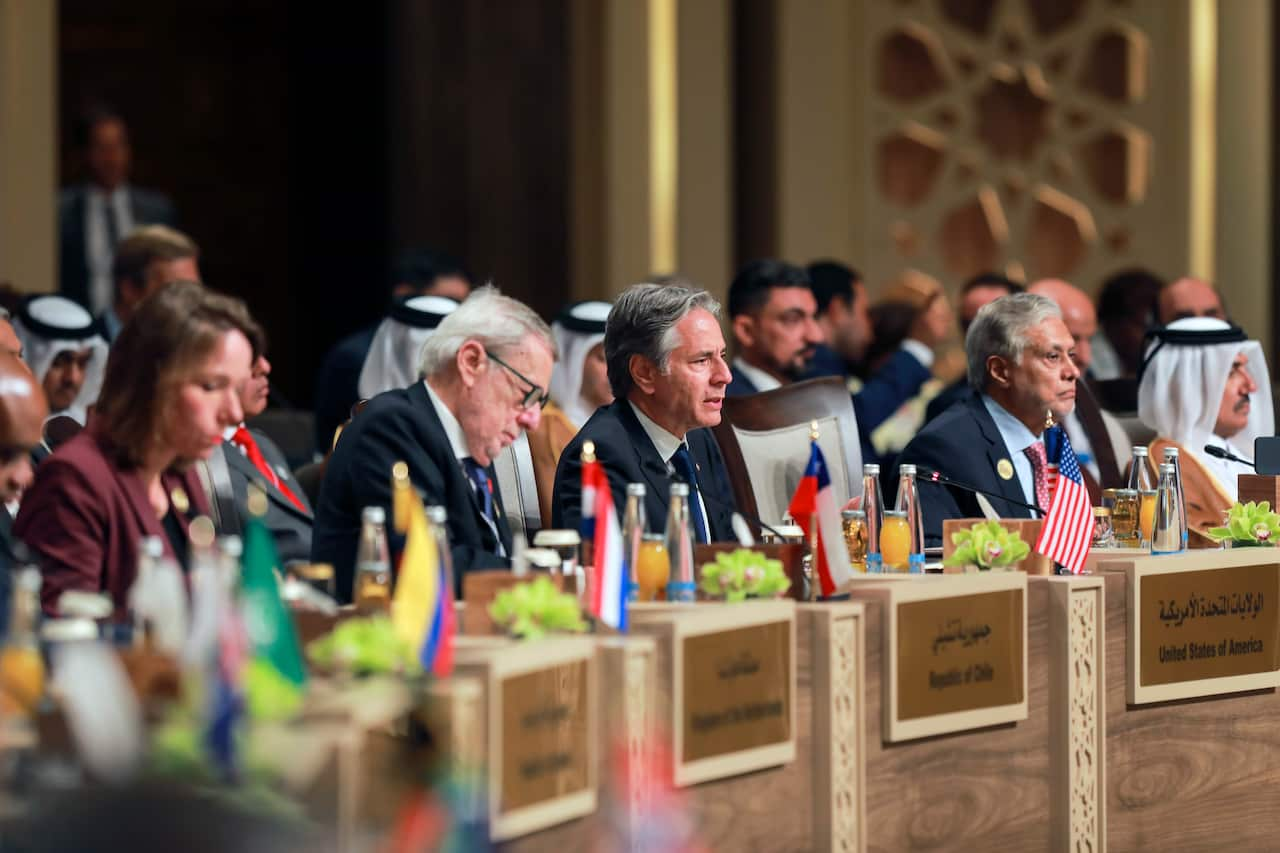 A group of people seated around separate sections of a round table. There are flags representing the various countries they're from on each section of table.