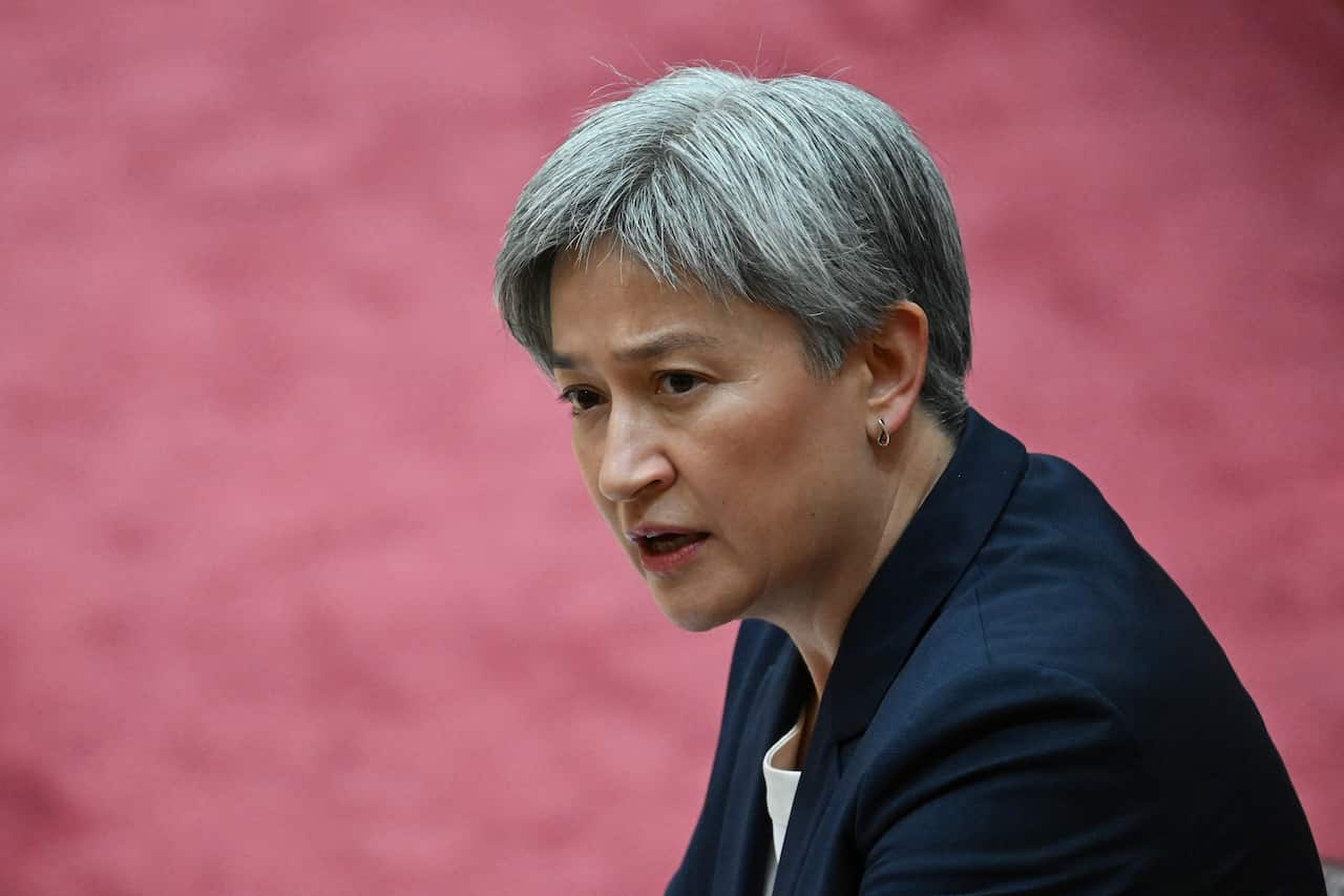 Penny Wong sitting down. A pink floor is visible in the background.