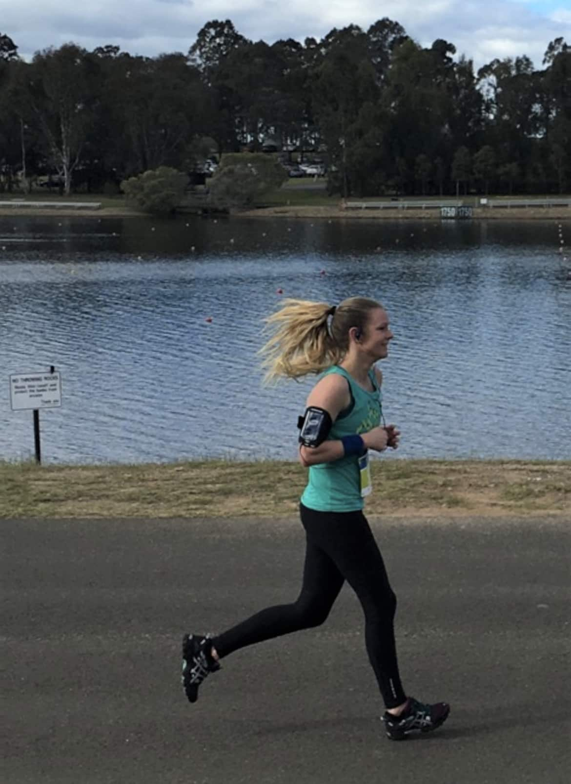 A woman in jogging gear runs along a pavement beside a river. 