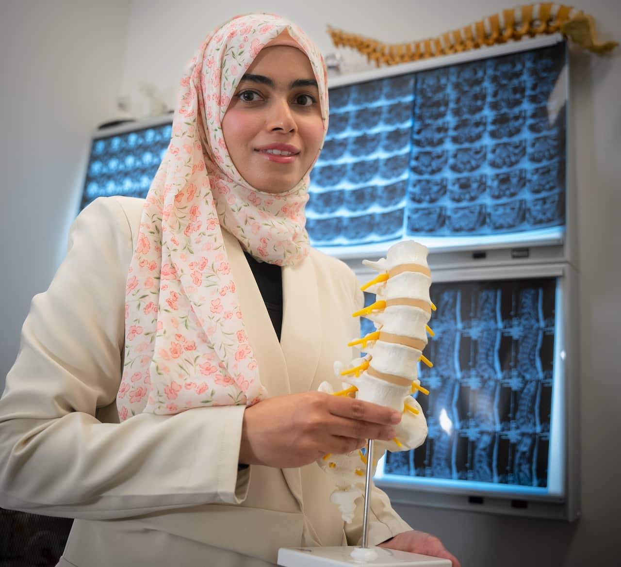 A woman wearing a headscarf holds a lumbar spine model. 