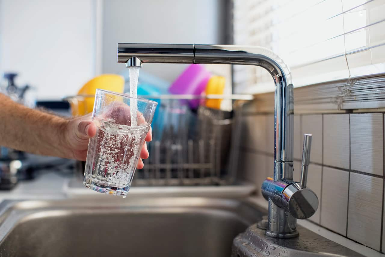 A man holding a glass of water under a kitchen sink tap.