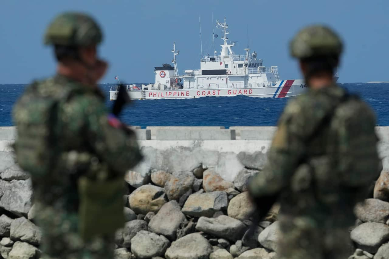 Two soldiers in green camouflage look on at a vessel in the sea that has "Philippine Coast Guard" written along its side. 