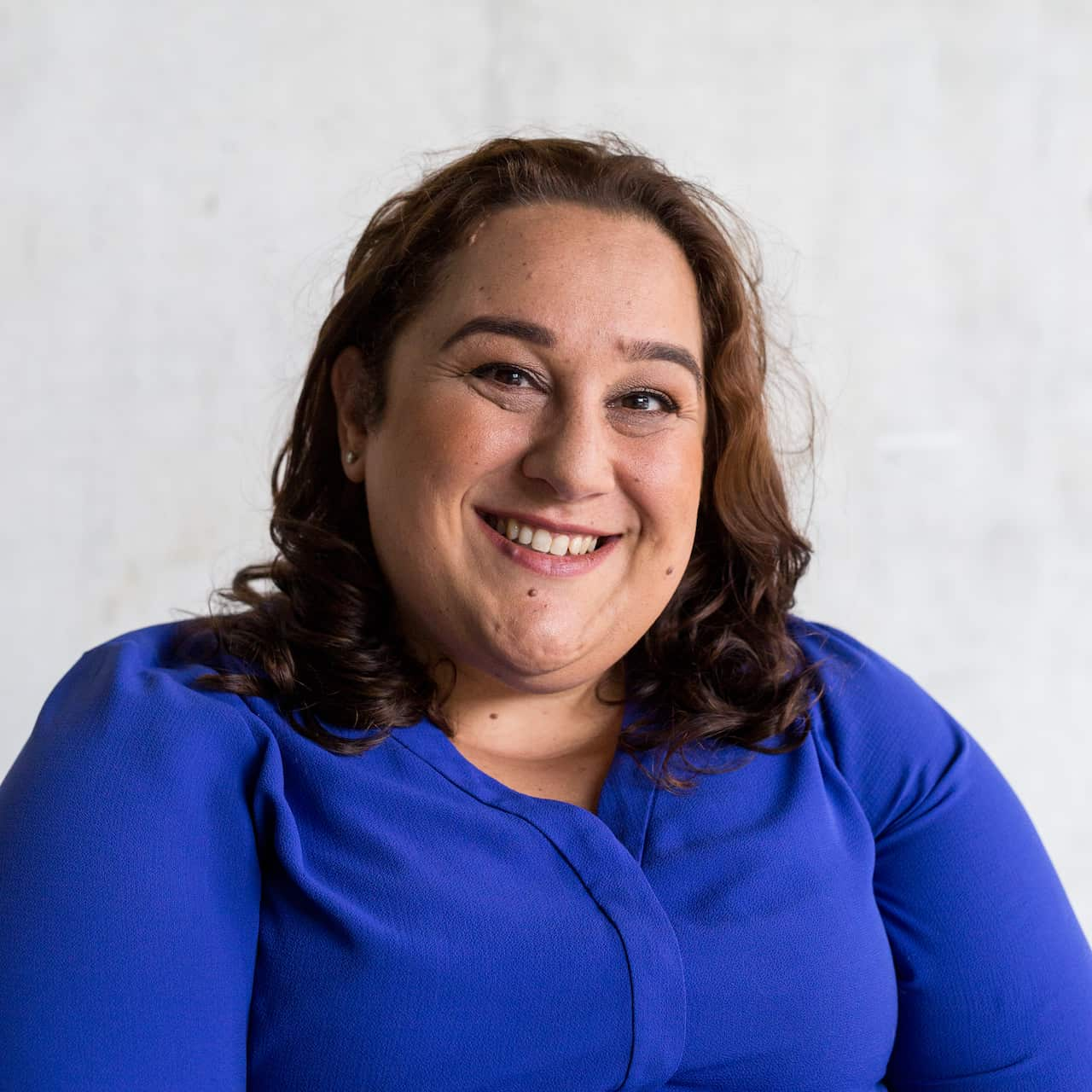 A woman in a blue top smiling in front of a grey background.