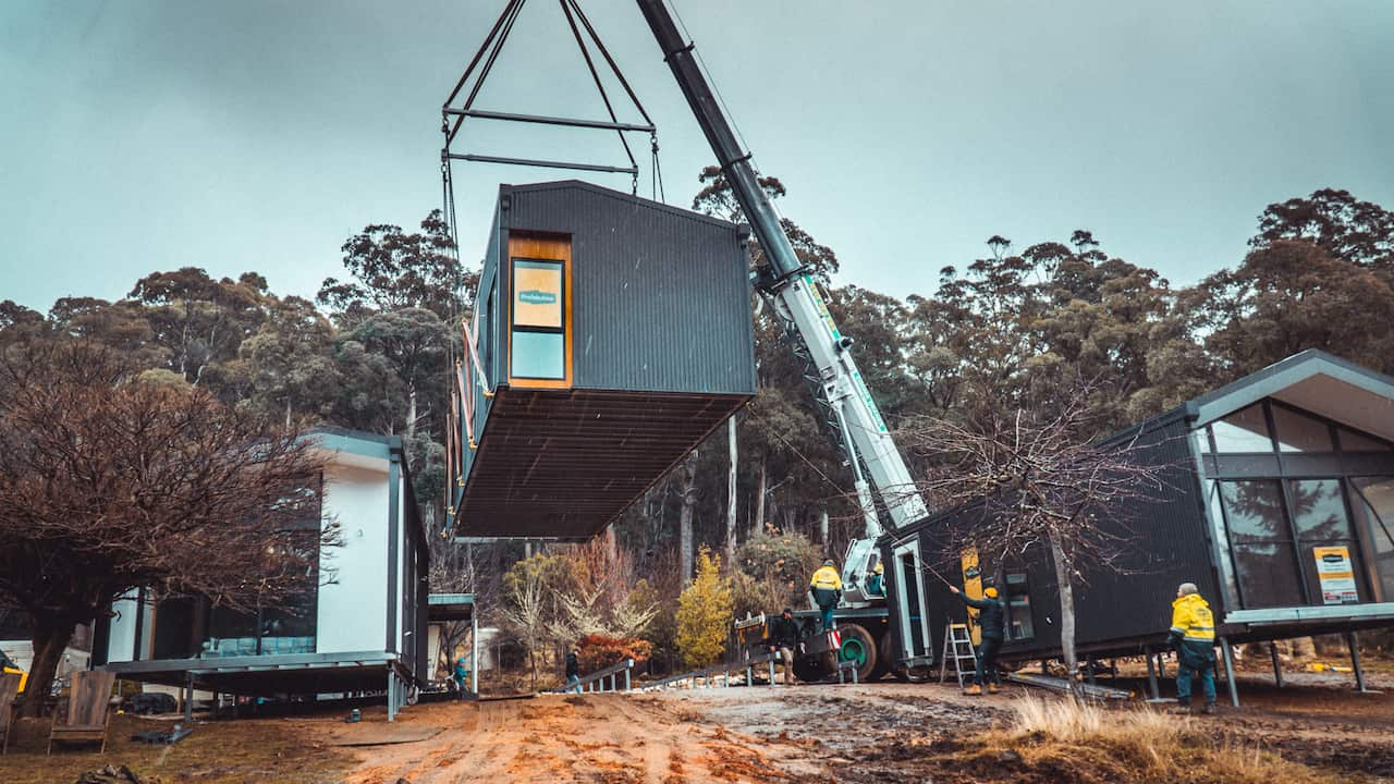 A crane raises a modular house in the air