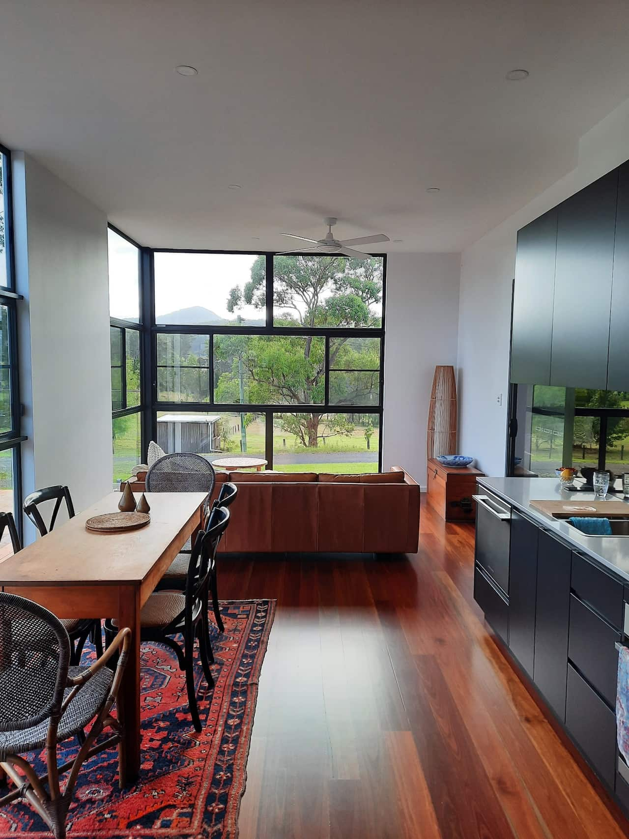 Interior shot of a kitchen, dining table and lounge with large windows overlooking green landscape