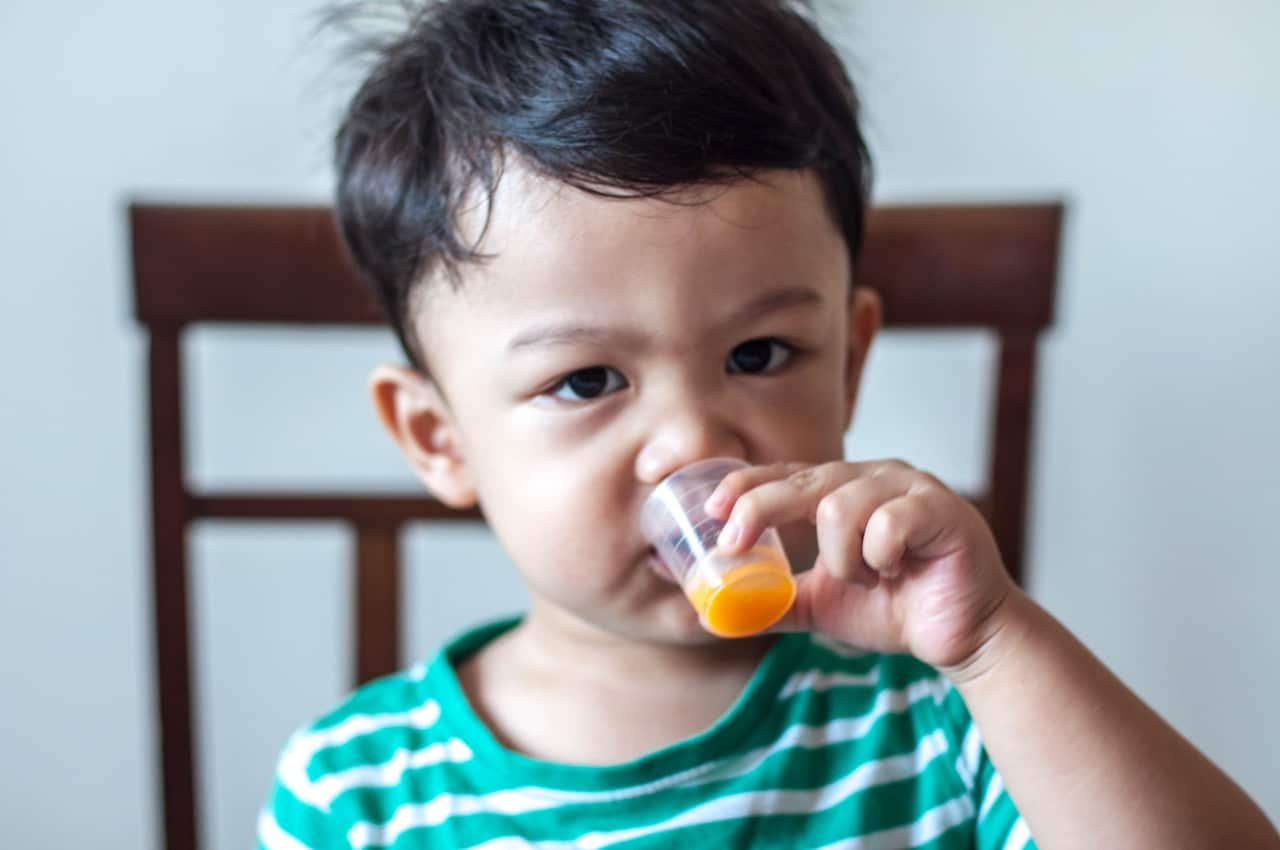 A male toddler is drinking medicine from a medicine cup.