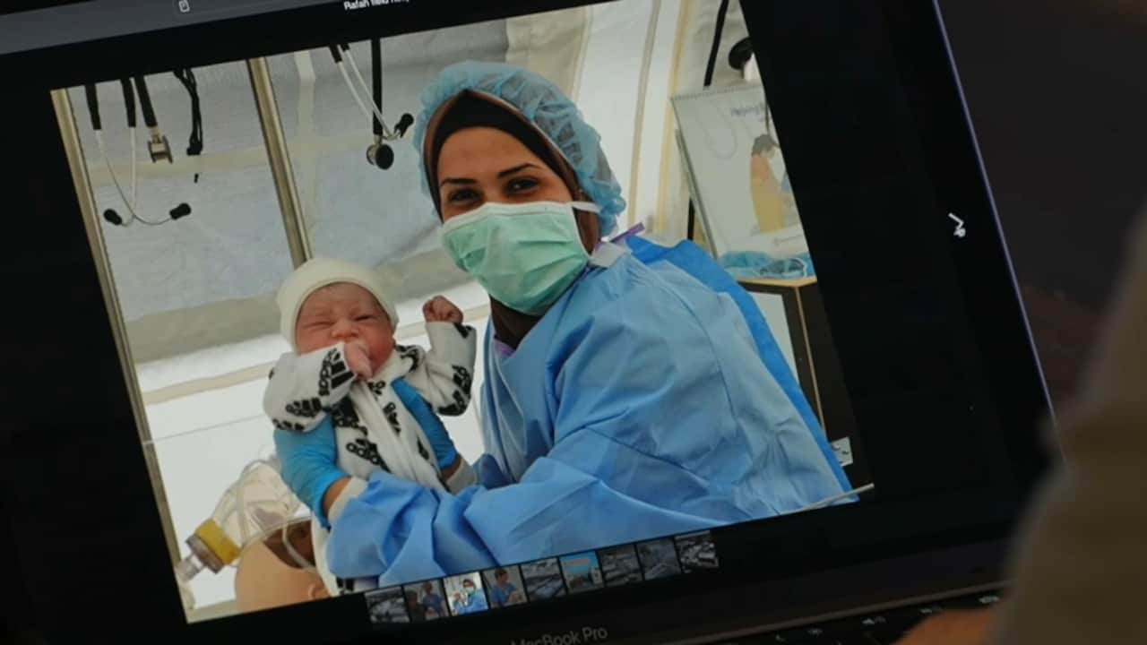 An image on a monitor of a nurse holding up a baby.