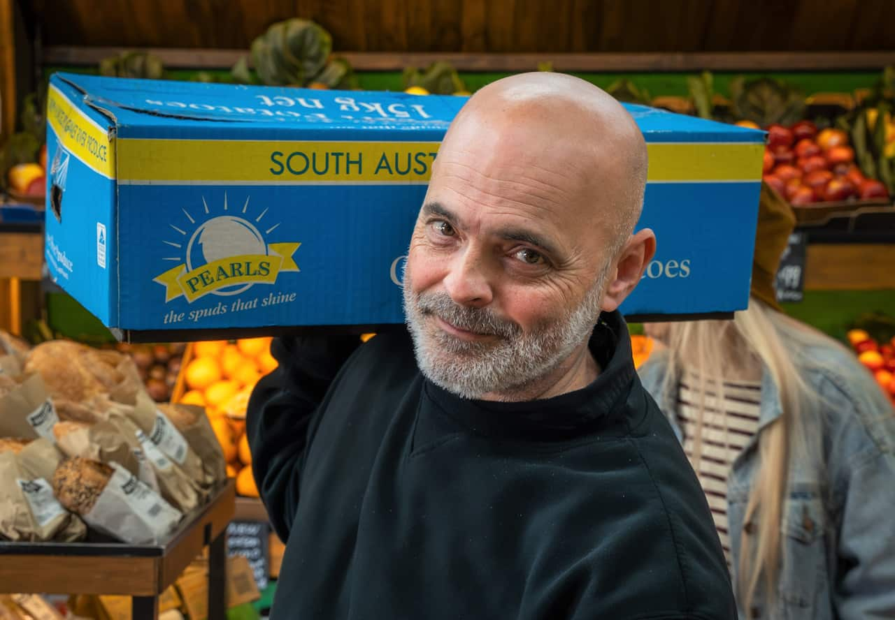 A man in a black sweater carrying  box of groceries inside a fruit shop.