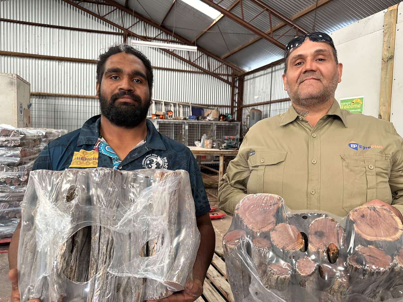 Two men hold bags of acacia chopped for firewood. 