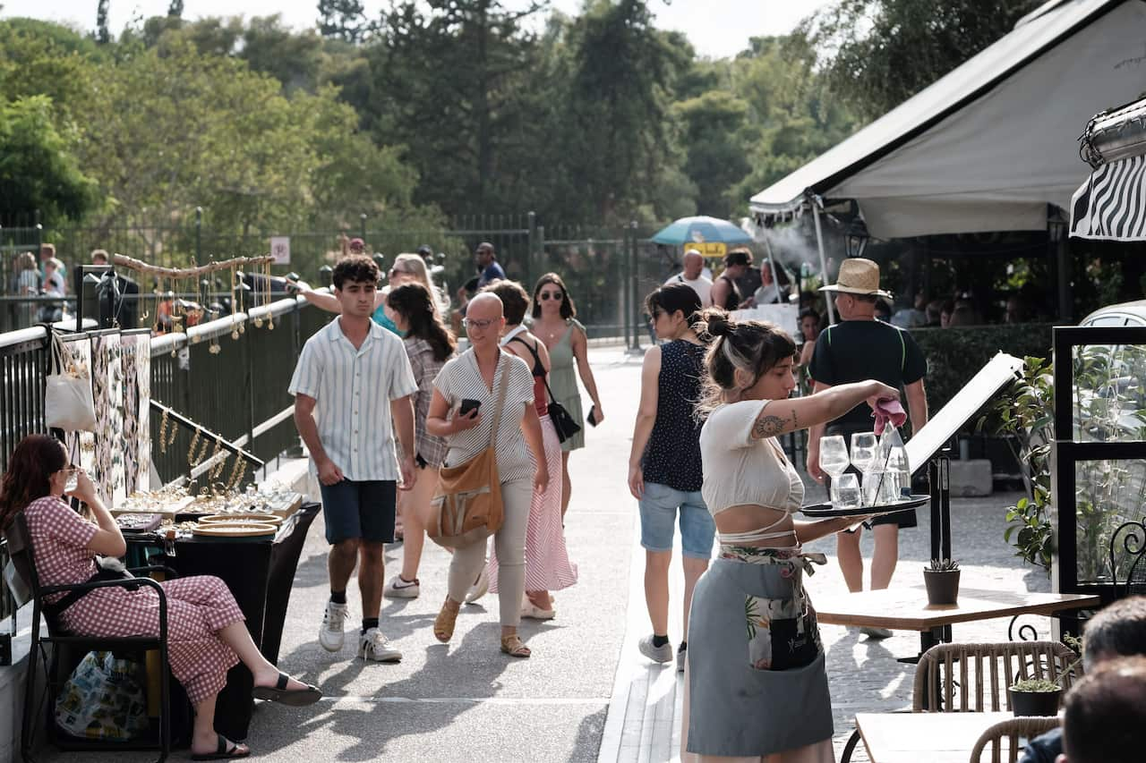 People walk through a terrace cafe where a waitress carries a tray.