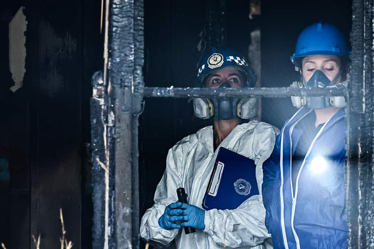 Two women wearing face masks inspect a building that has been damaged by fire.