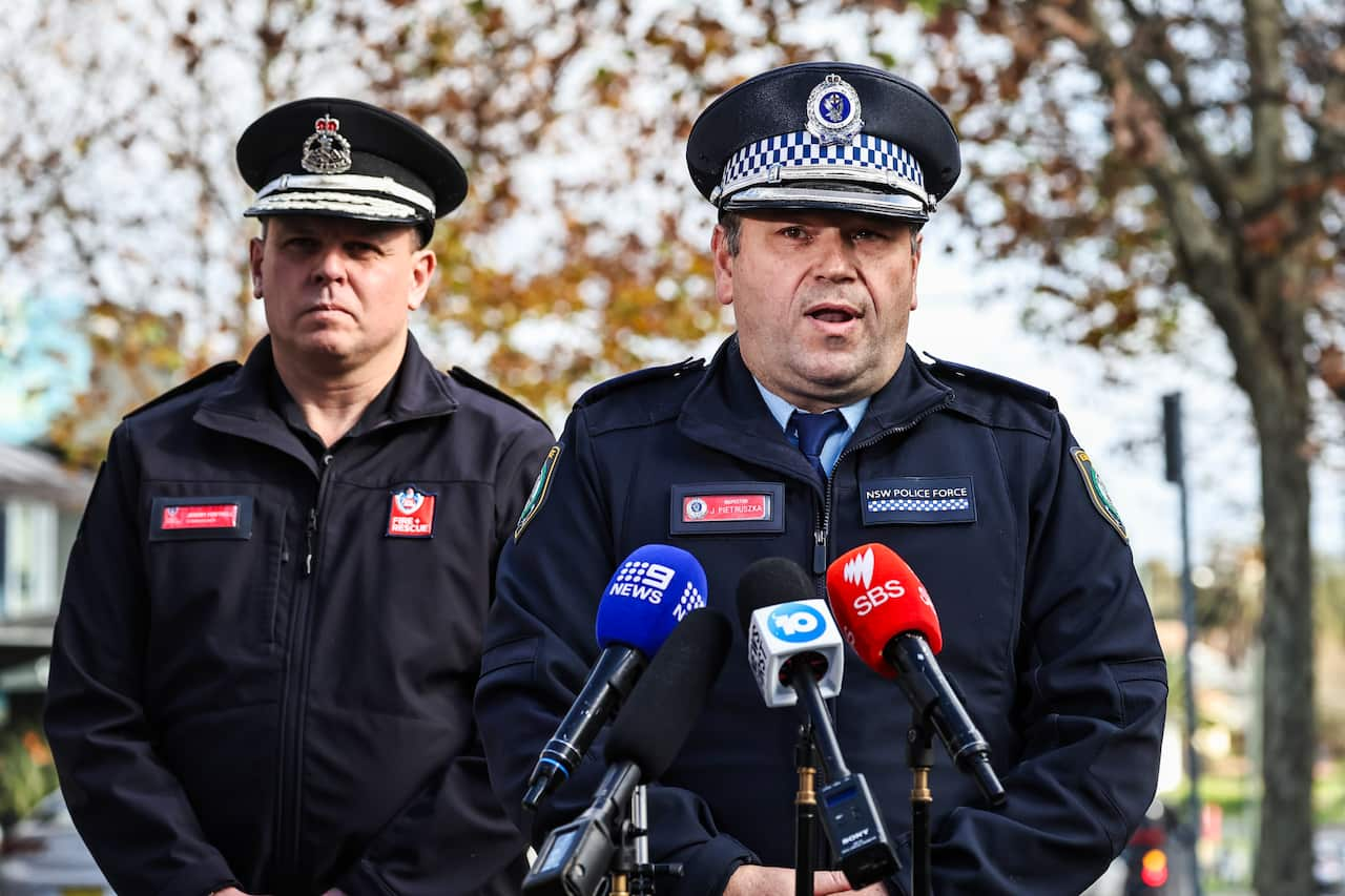 A police officer speaking into media microphones. A Fire and Rescue officer is next to him.