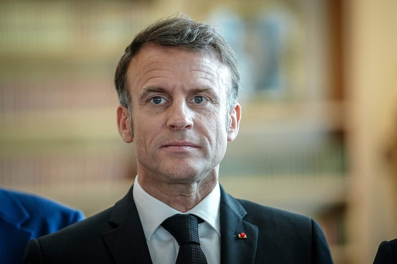 French President Emmanuel Macron in a suit in front of a brown wall.