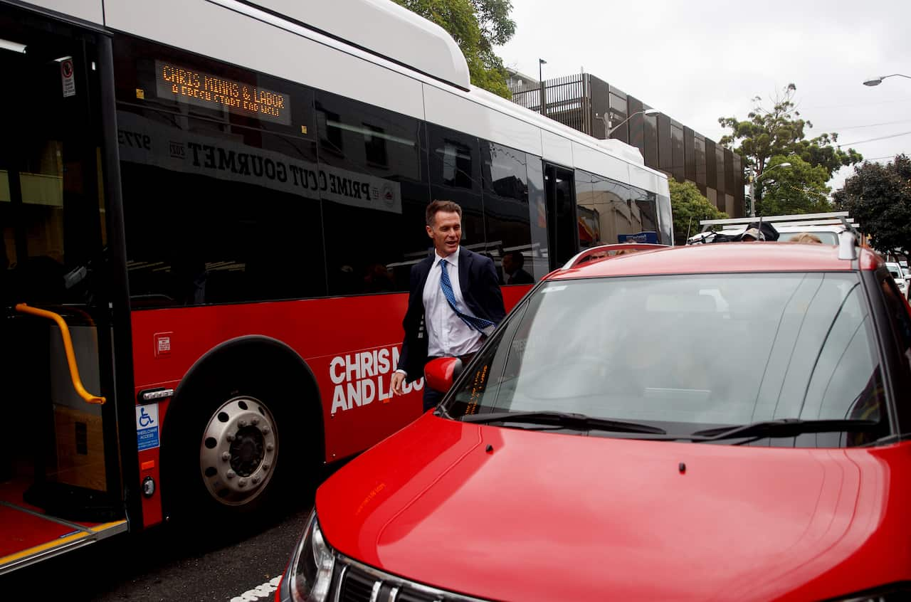 NSW Premier Chris Minns  standing on a road in between a bus and a parked red car.