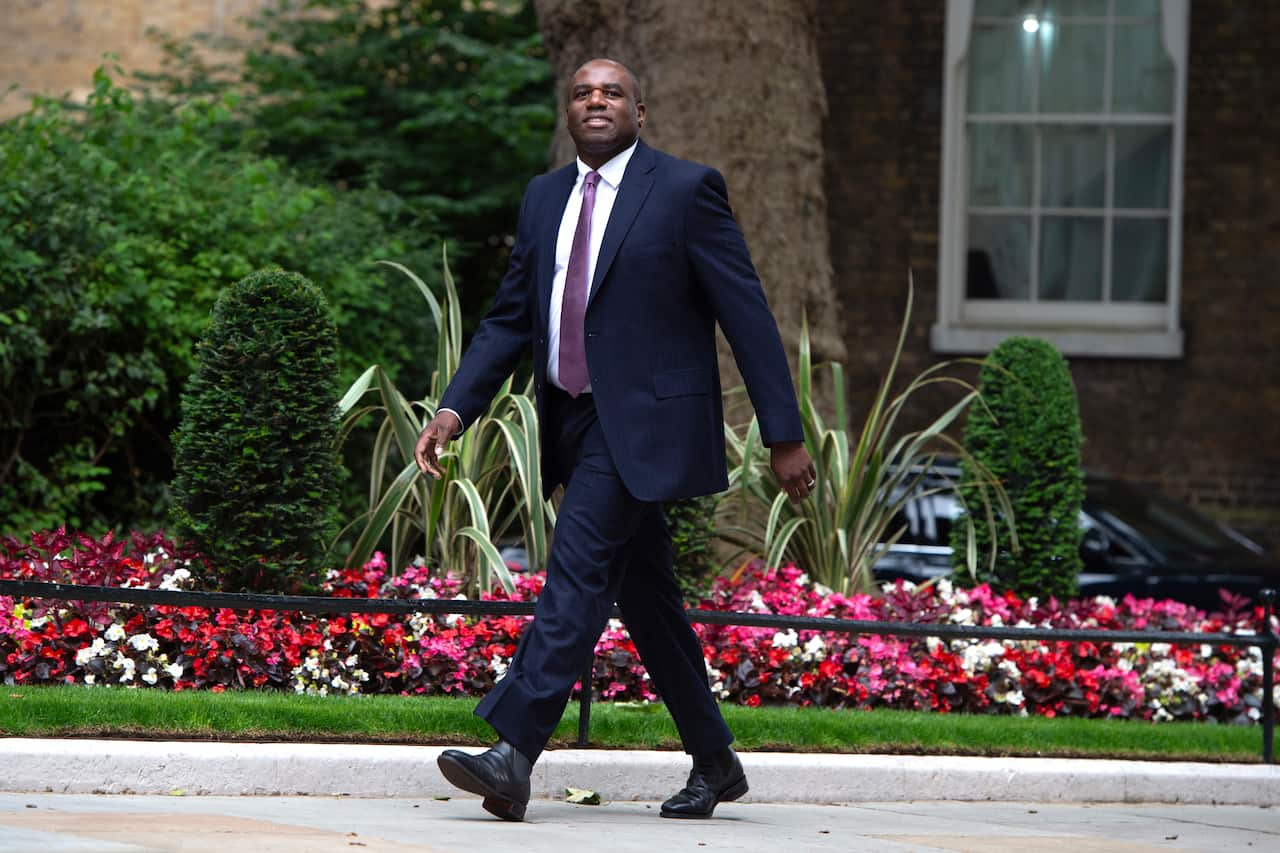 A man in a blue suit walking in front of flowers.