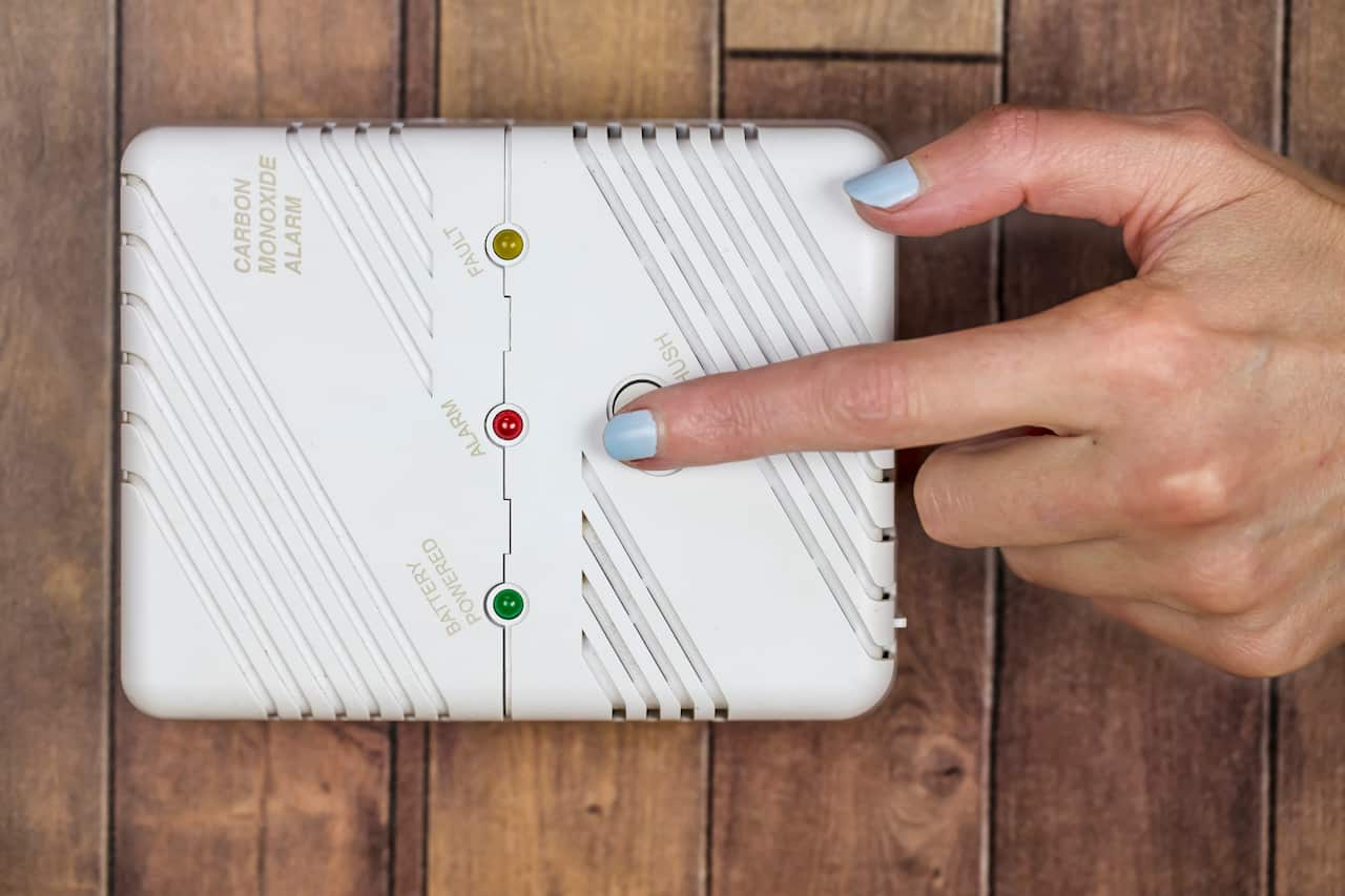 A person using their finger to press on a carbon monoxide alarm.