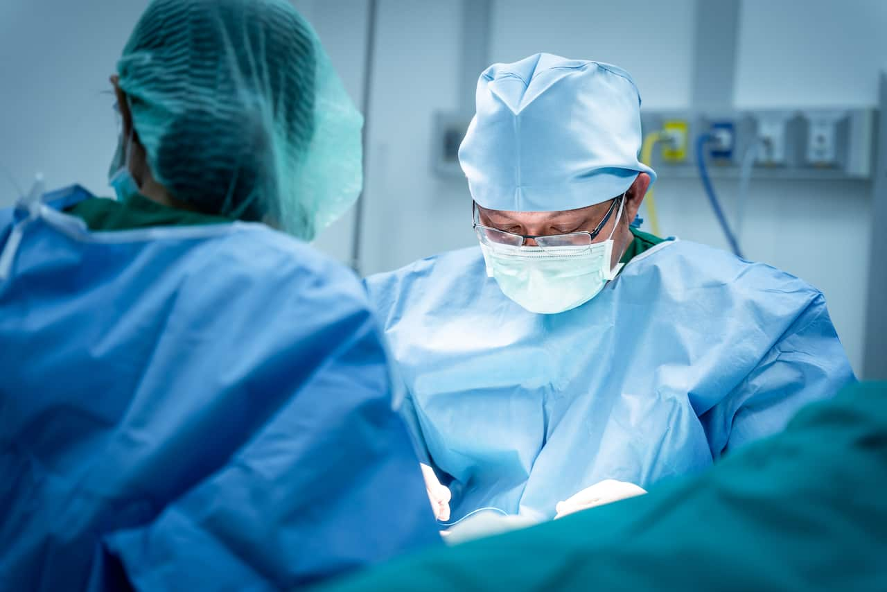 Two surgeons in blue scrubs operate on a person