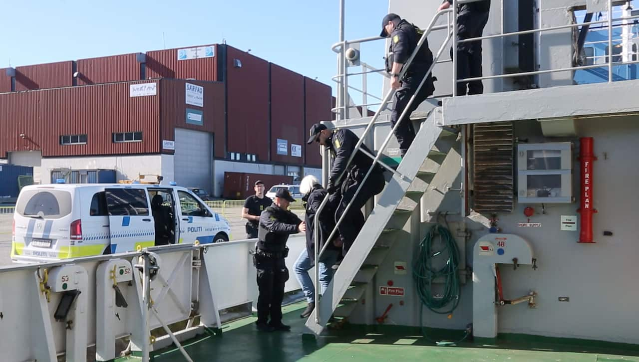 Danish police officers arrest a man on a boat, docked in a harbour.