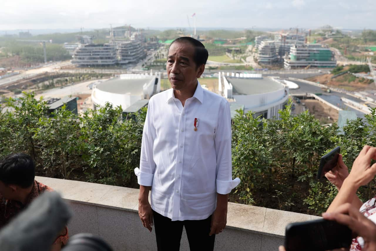 A man in a white shirt on a balcony overlooking a city under construction 