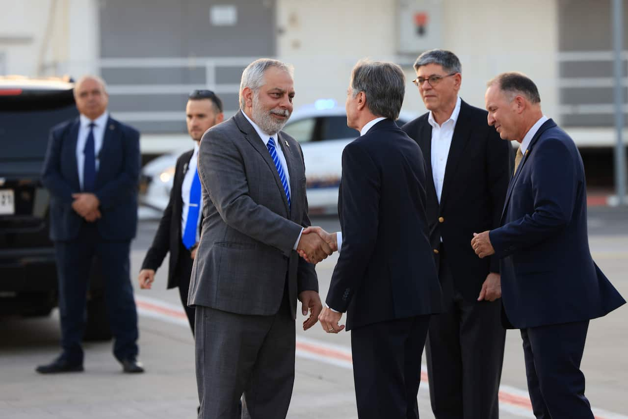 Two men in suits shake hands while two others stand in the background.