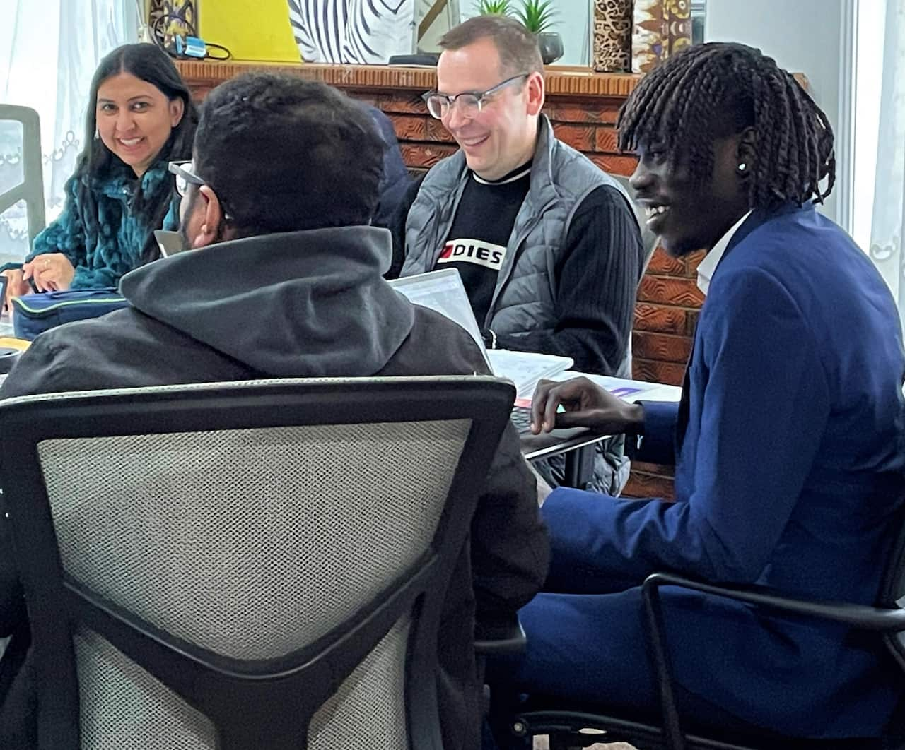 A man in a blue blazer sits at a table with others working on computers.