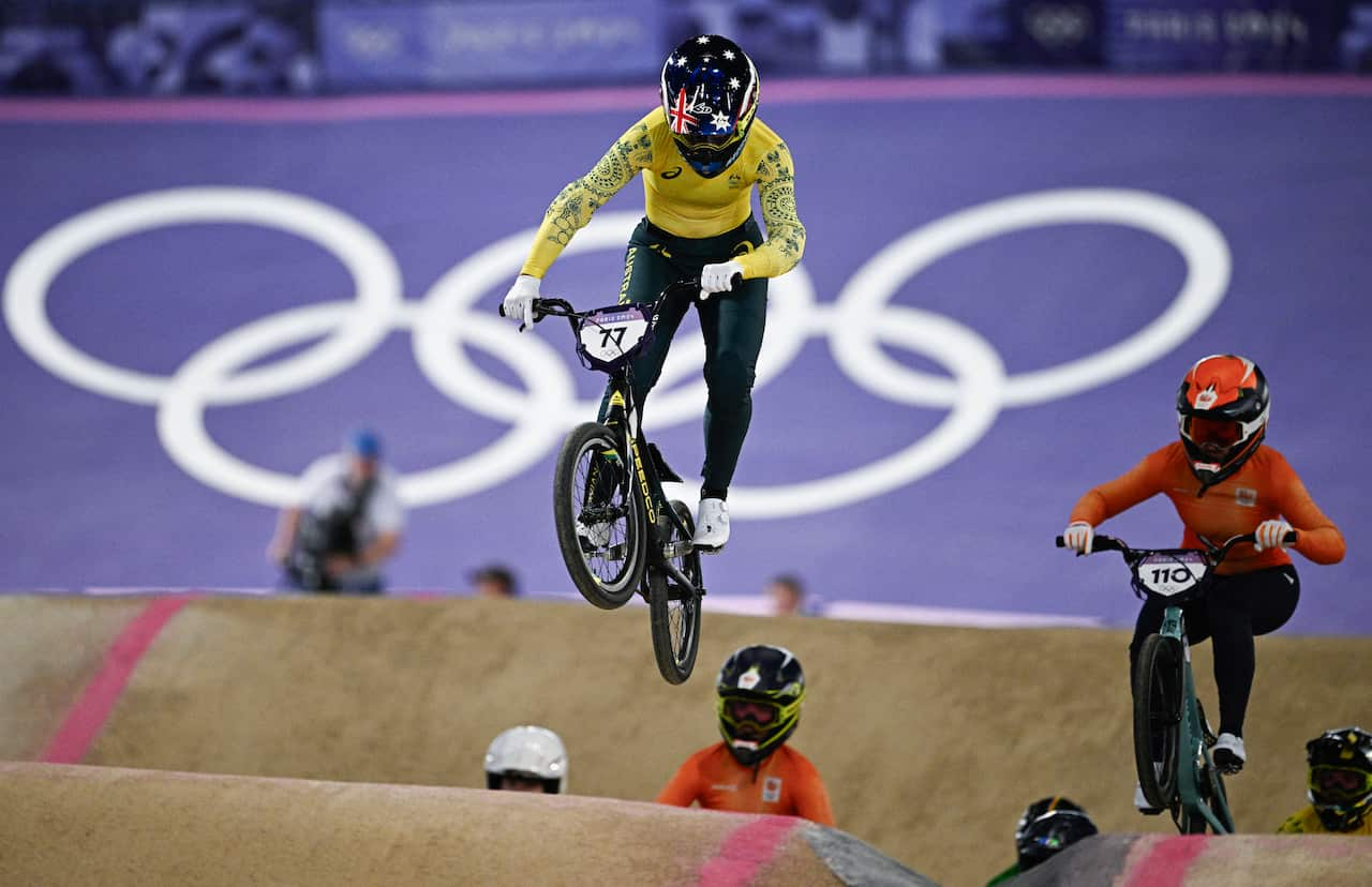 Women with helmets riding on BMX bicycles during an Olympic event.