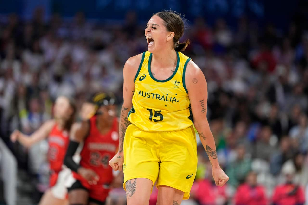 A woman in a bright yellow Australian basketball uniform looks joyous inside a basketball stadium.