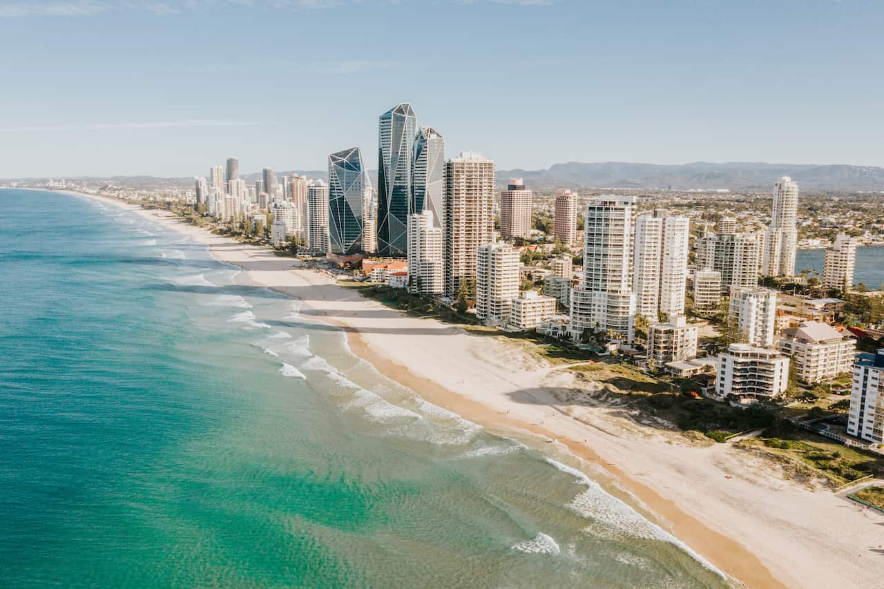 A calm beach of clear water breaks on white sand below tall white buildings of the Gold Coast.