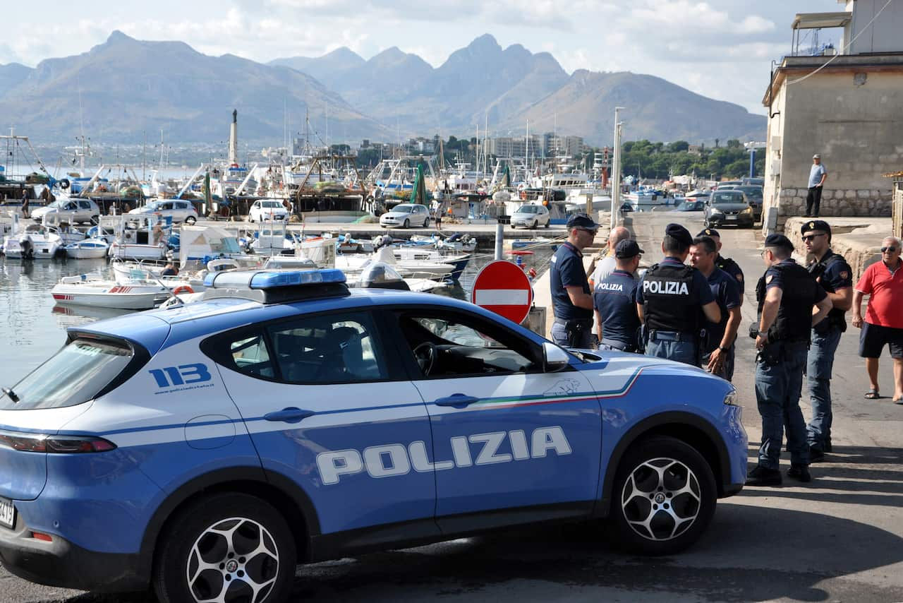 A group of police officers stand next to a blue Italian police car.