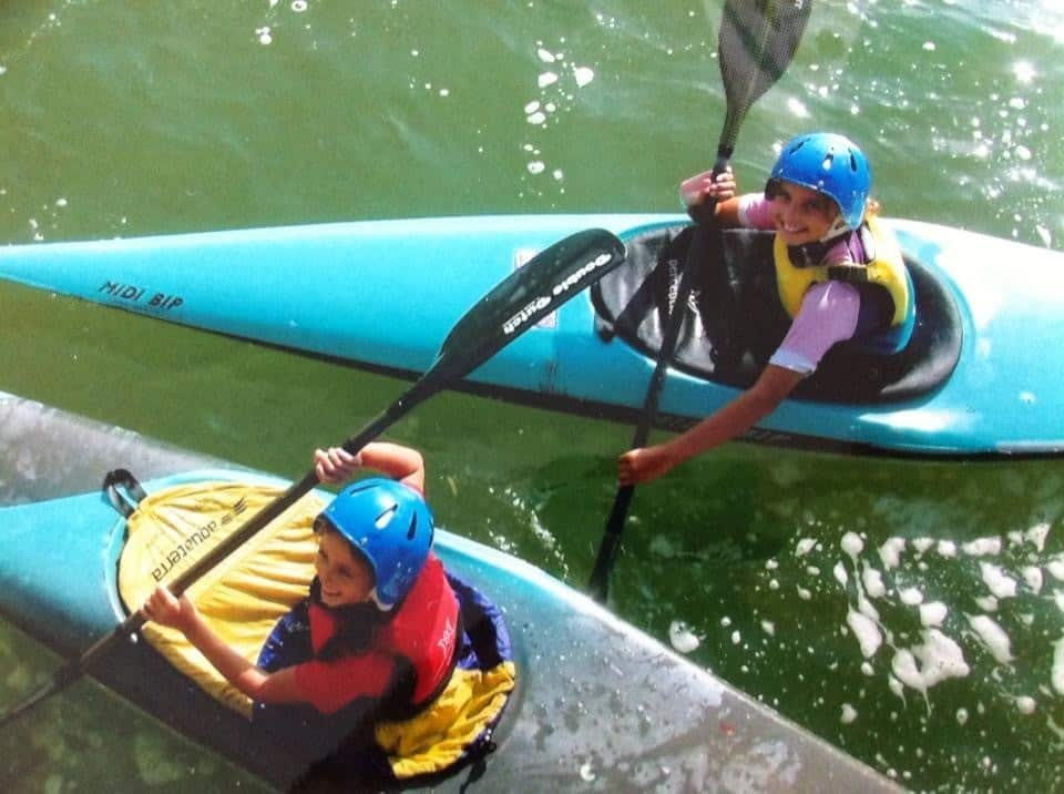 Two girls in kayaks look up towards the camera