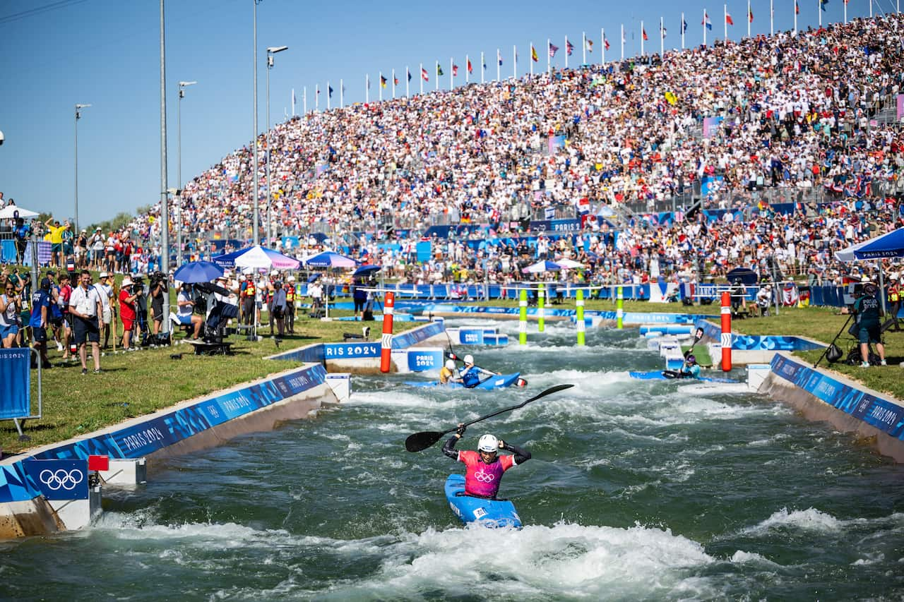 Women in canoes on the water with a stand of spectators behind them. 