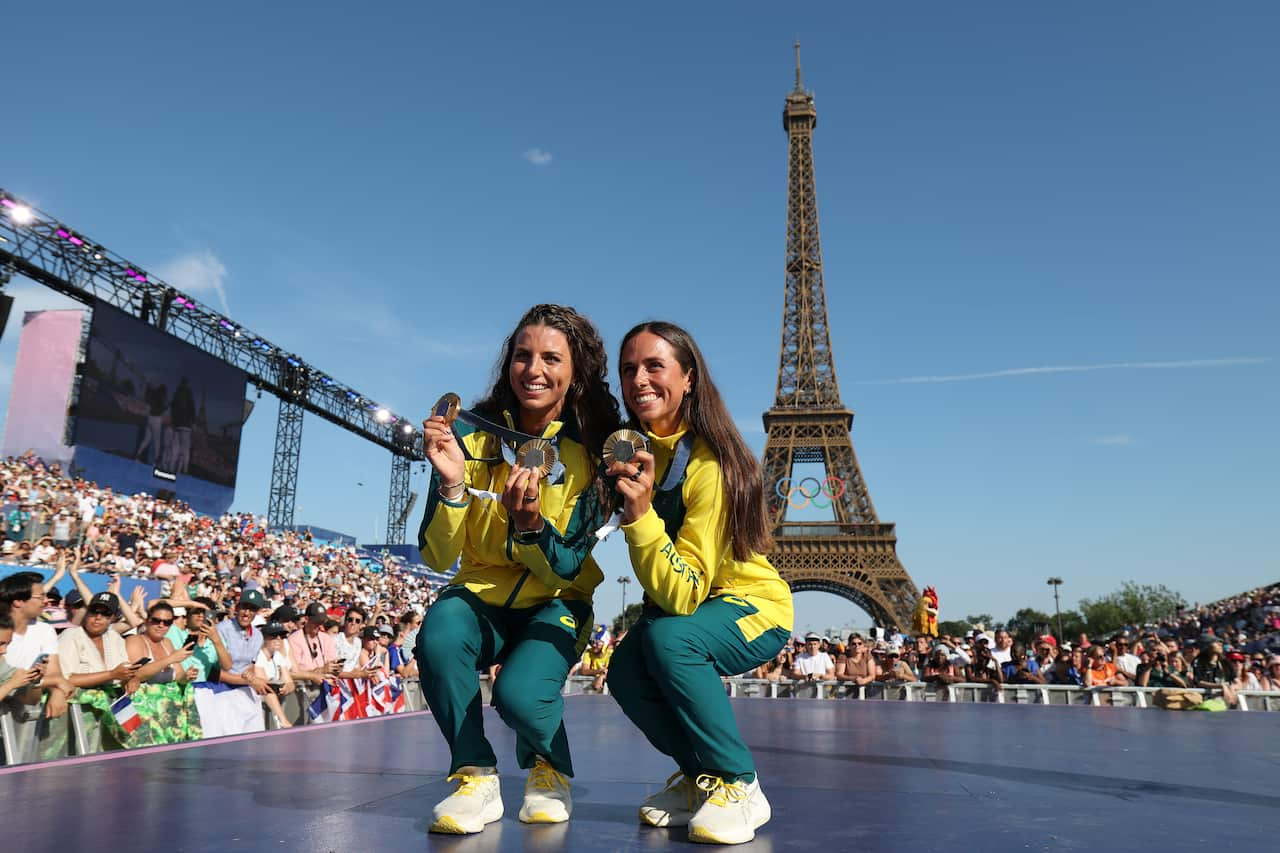 Two women wearing green and yellow tracksuits, pose with their gold medals with the Eiffel Tower in the background.