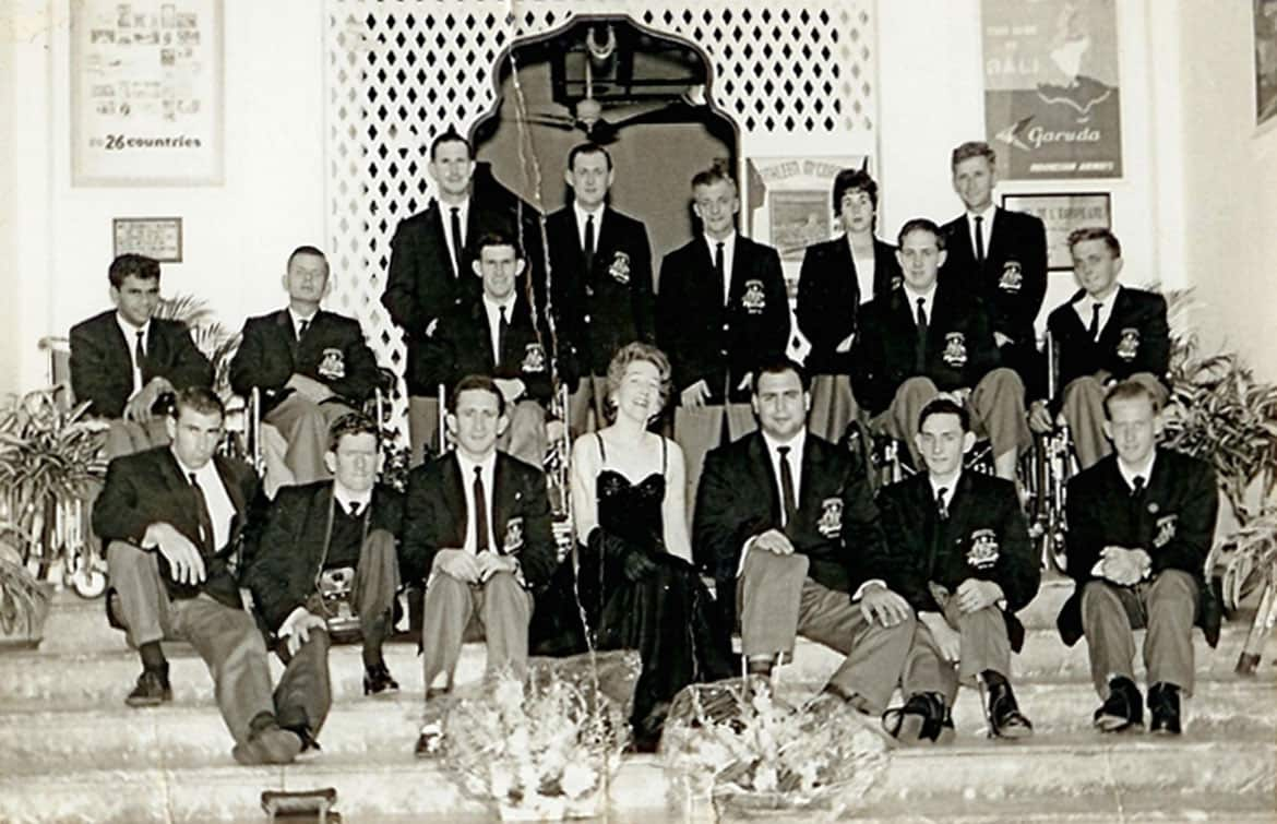 A black and white picture of men in trousers and blazers. There I a woman at the front in a formal gown and another at the back in a black suit and white top